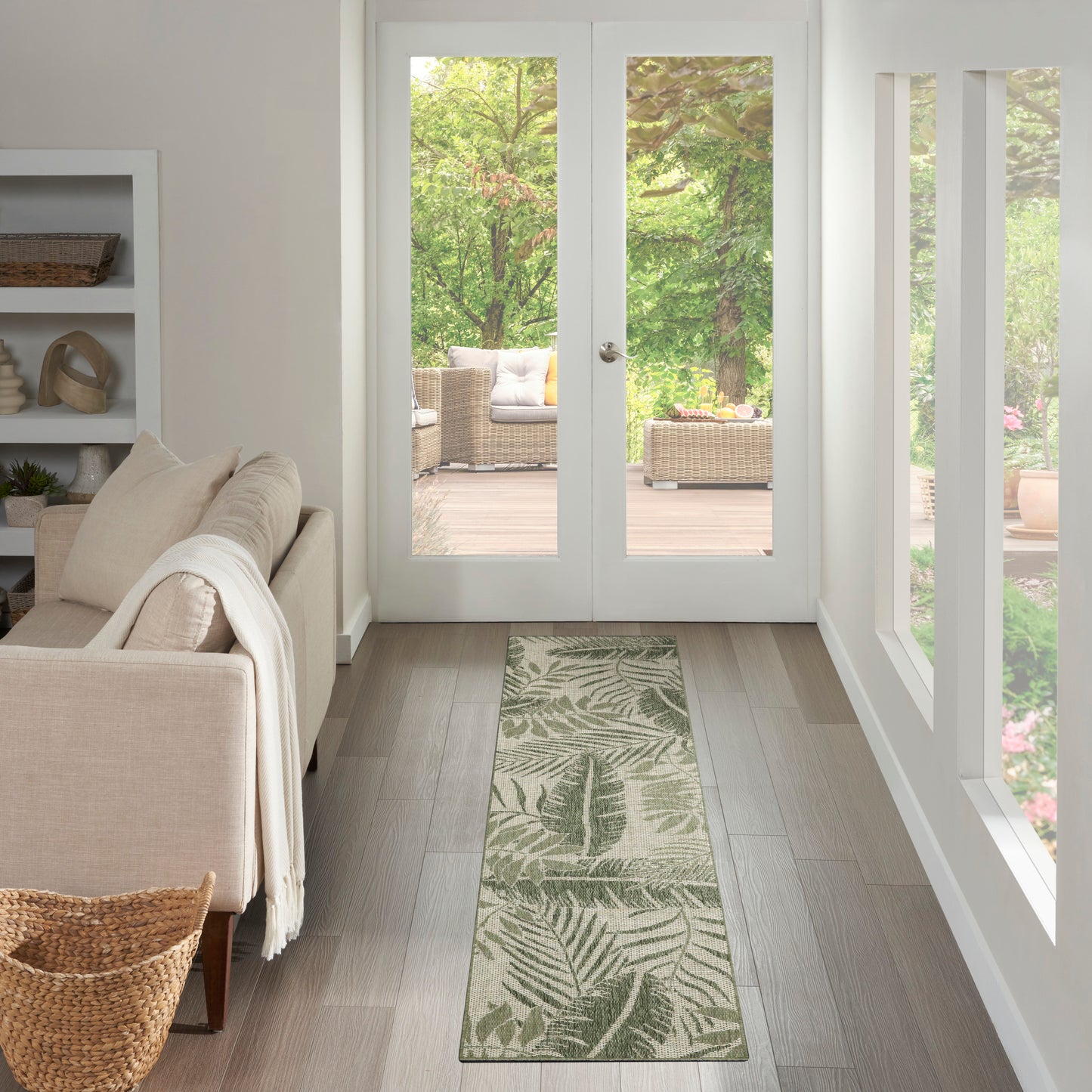 Outdoor 6' runner rug with a fern-patterned green design on light patio flooring near glass doors opening to a garden.