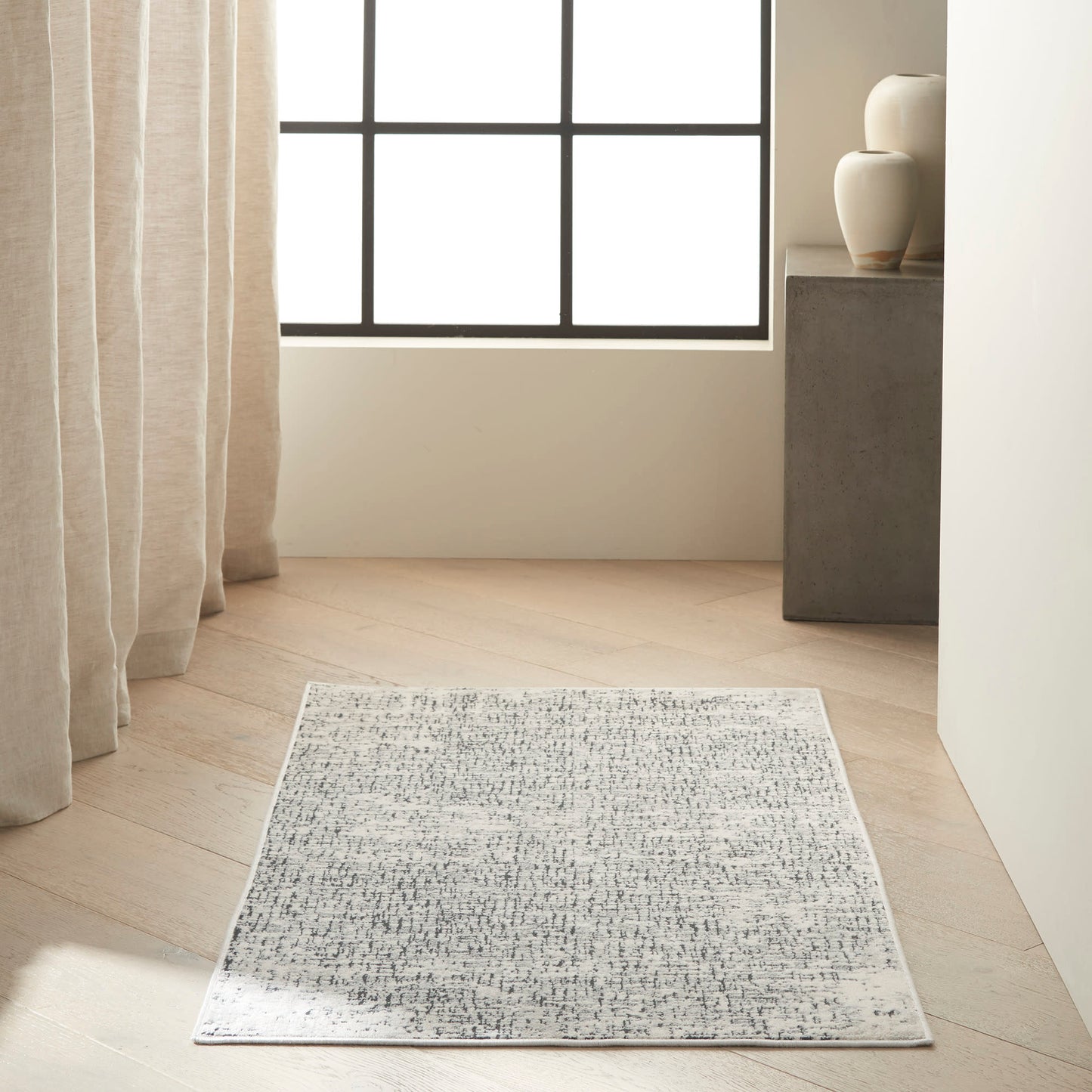 Rectangular grey and white abstract-pattern rug, low-pile, laid on light wood floor in a bright minimalist living room.
