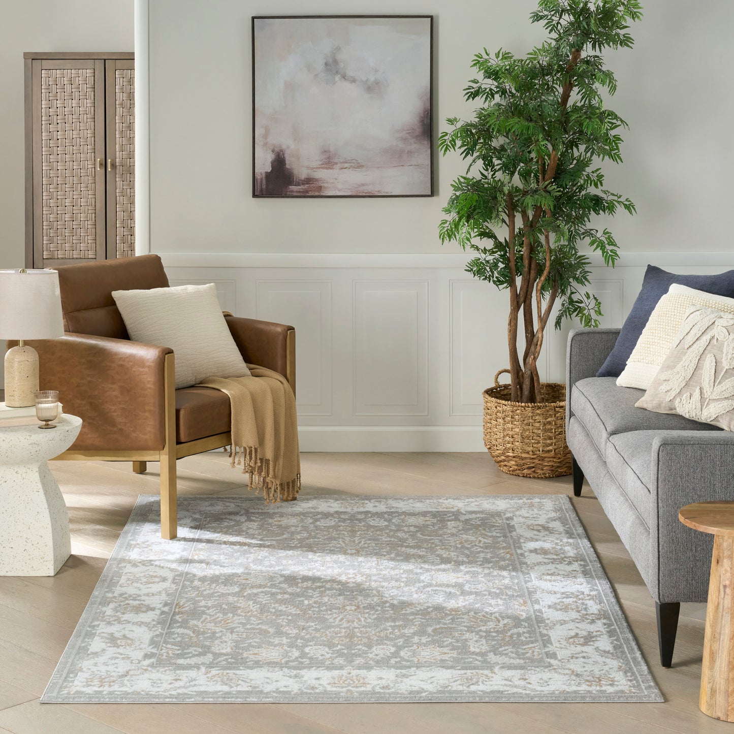 Rectangular distressed gray-ivory area rug under living room seating with brown leather chair, gray sofa, and potted tree.