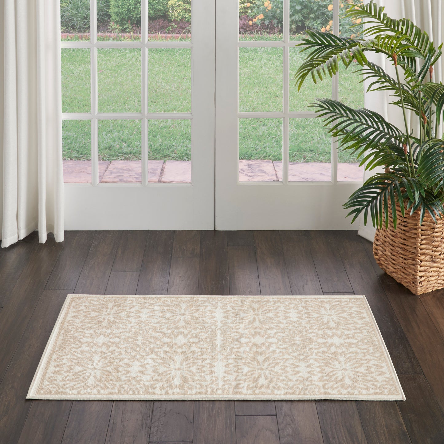 Beige patterned area rug on dark hardwood floor in front of glass French doors; potted palm in wicker basket to the right.