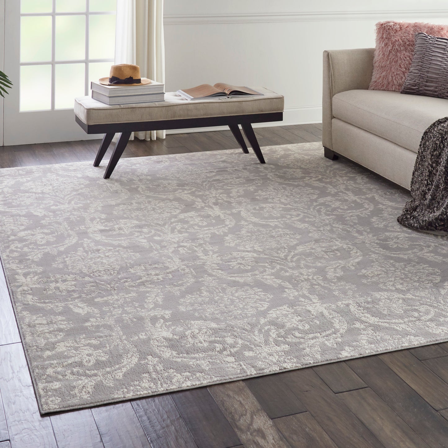 Light gray damask-patterned area rug (7' x 10') on dark wood flooring, paired with a beige sofa and a low rectangular coffee table.