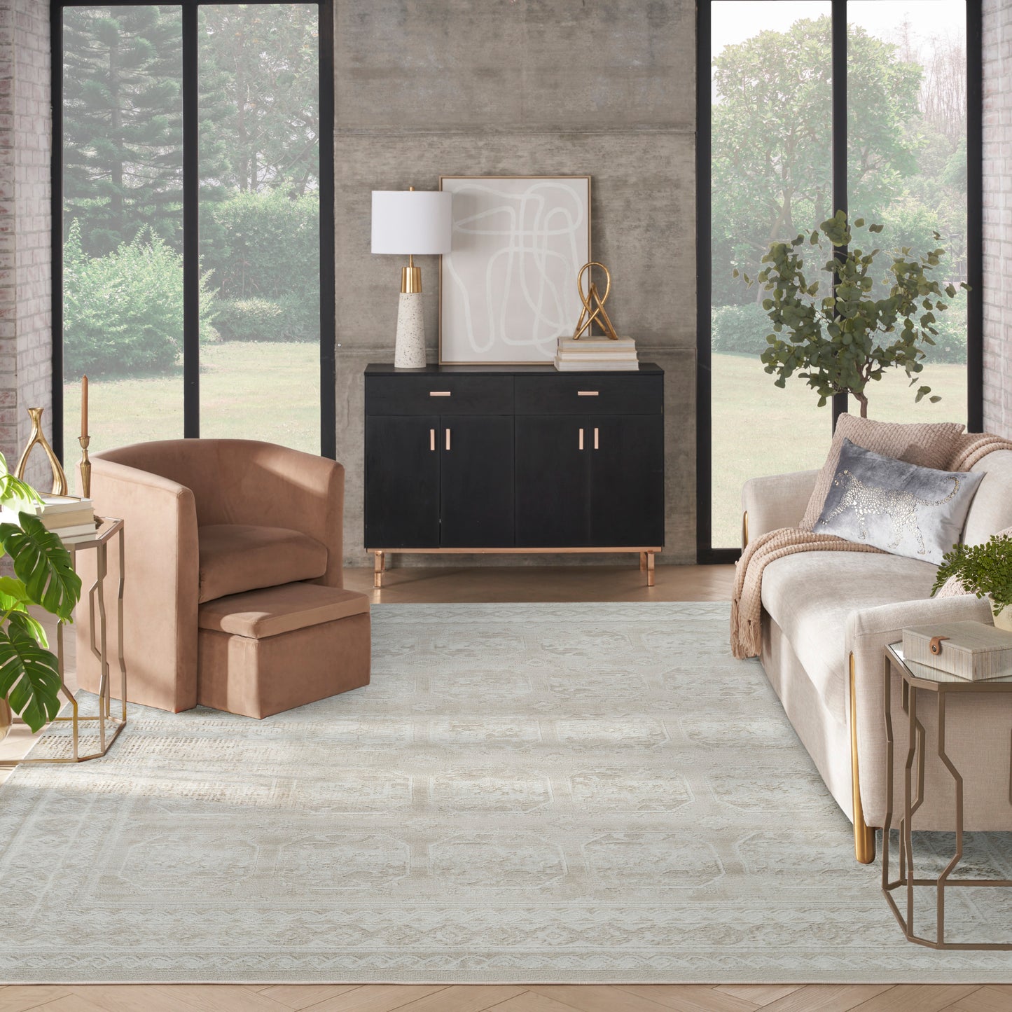 Bright, modern living room with a black cabinet, tan armchair, beige sofa, light patterned rug, large windows, greenery.