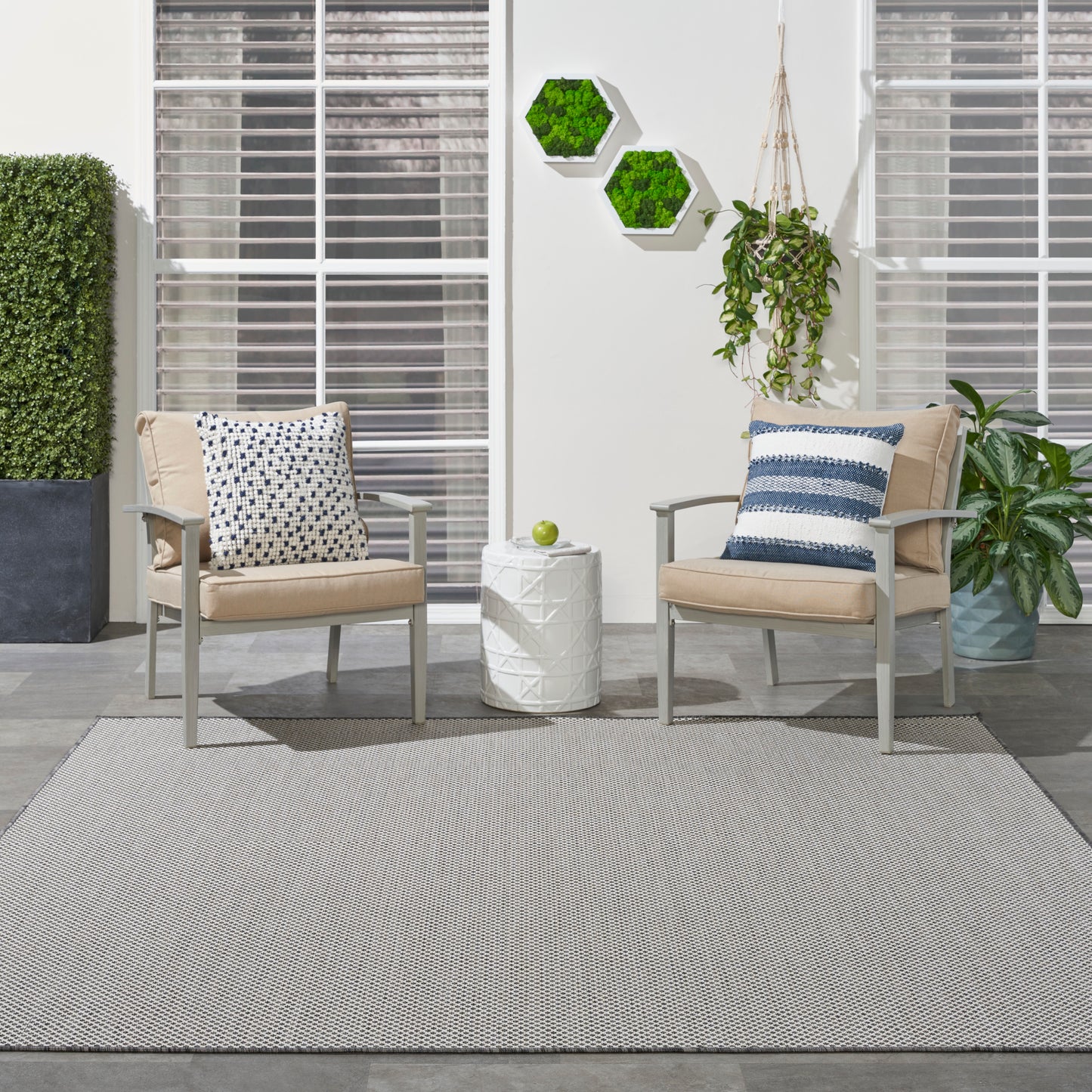Two beige outdoor lounge chairs with metal frames and patterned cushions flank a white geometric side table on a gray rug.