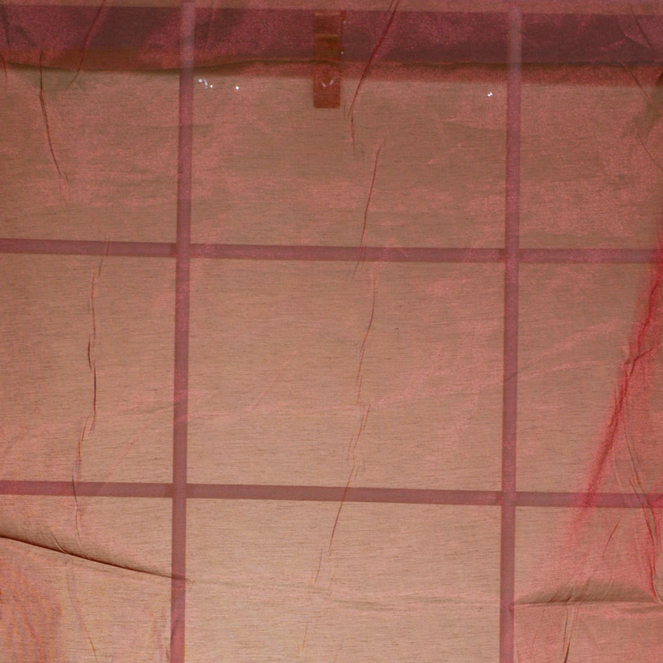 Pink-tinted beige drapery fabric with a grid of dark brown crossbars forming square sections; slight fabric creases.
