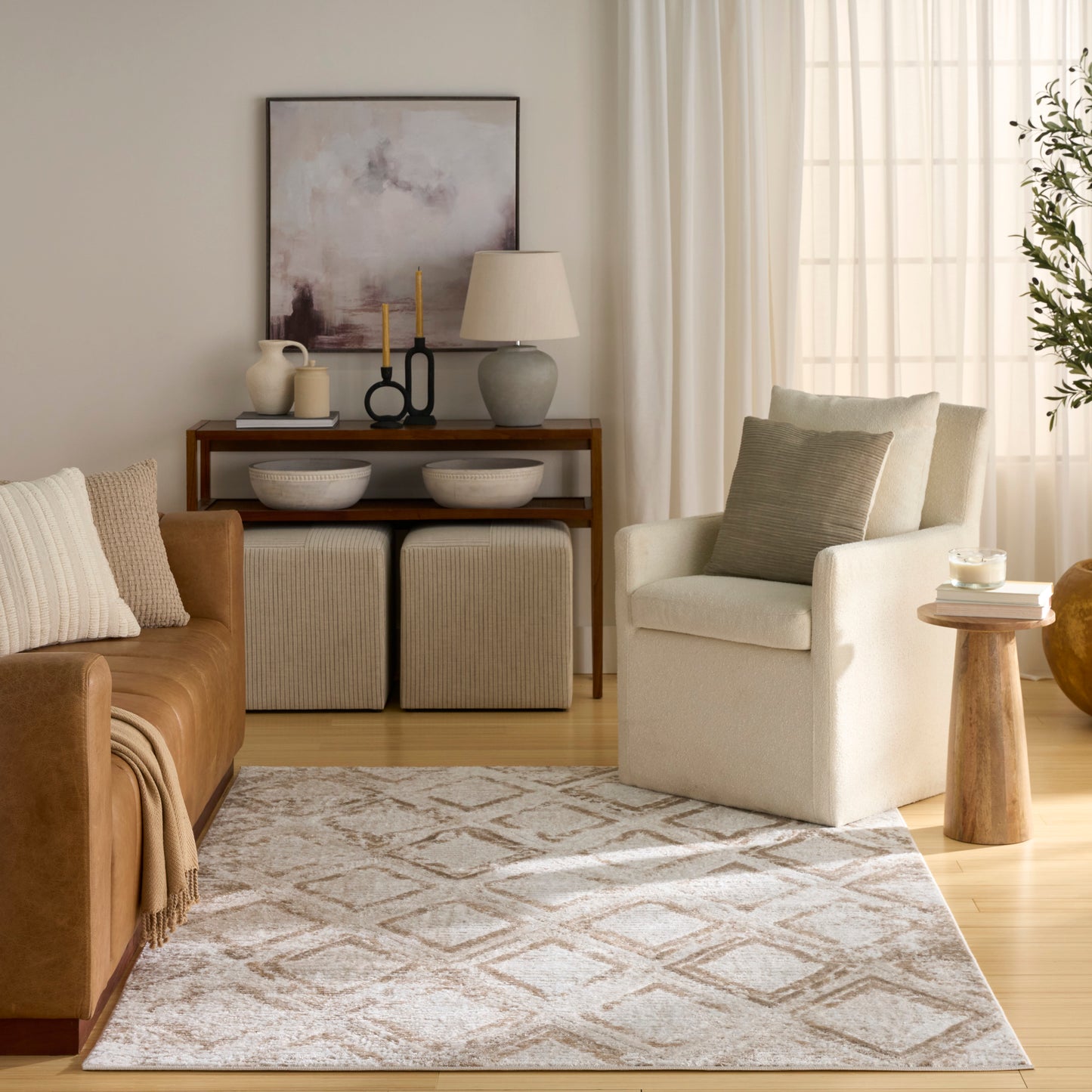 Neutral living room with brown leather sofa, cream armchair, beige geometric rug, wooden console with bowls, lamp and art.