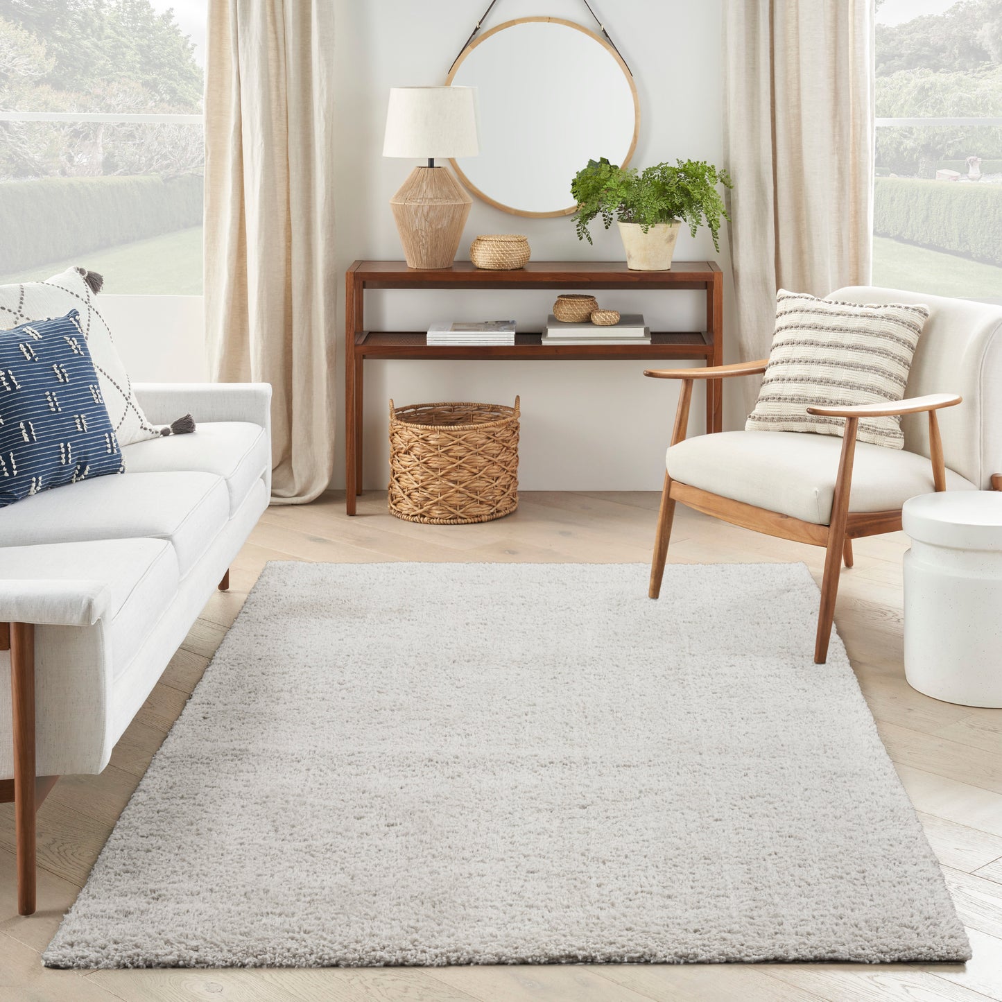Neutral living room with light shag rug, cream sofa, mid-century wooden chair, round mirror, plant, and wicker basket.