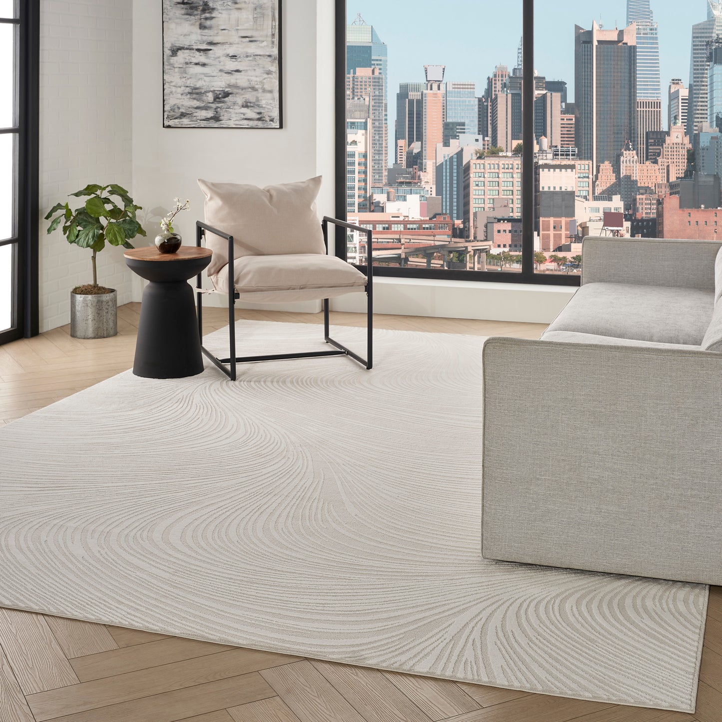 Modern living room: beige armchair with black metal frame, black wood-top side table, potted plant, cream swirl rug, city skyline view.