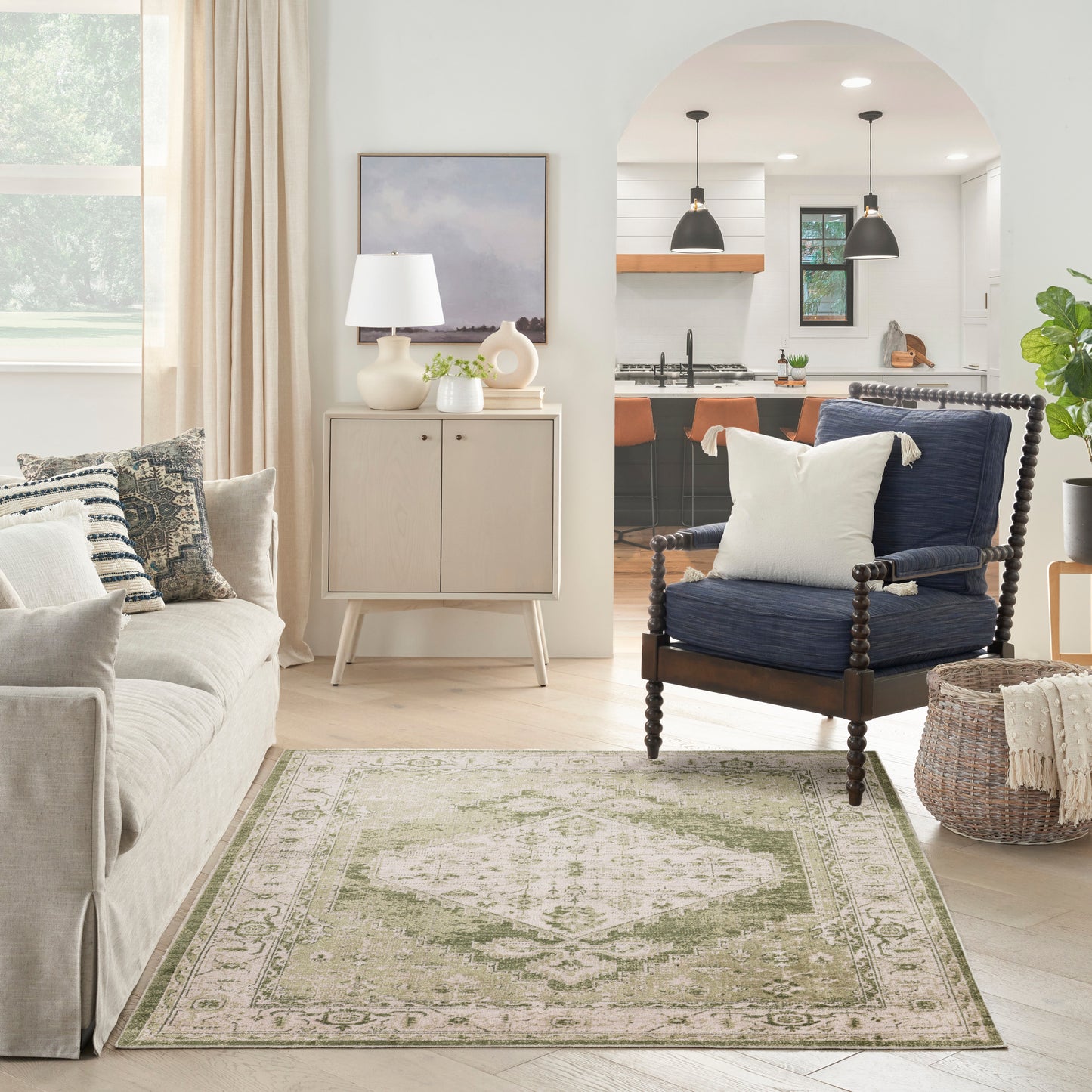 Neutral living room with beige sofa, pale green rug, dark wood spindle chair, light wood cabinet, arched kitchen opening.