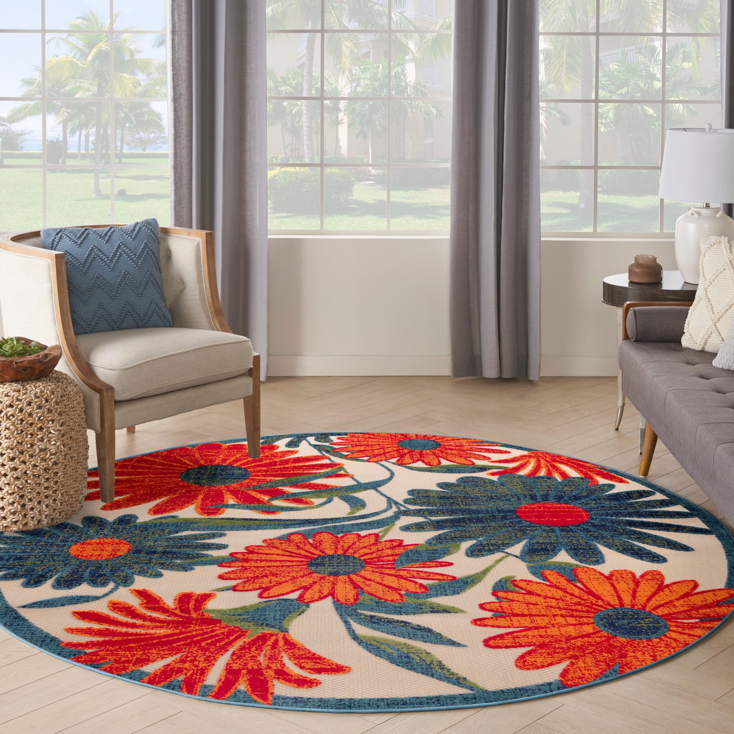 Round floral area rug with bold red, orange and blue flowers on beige backdrop and teal border; bright living room.