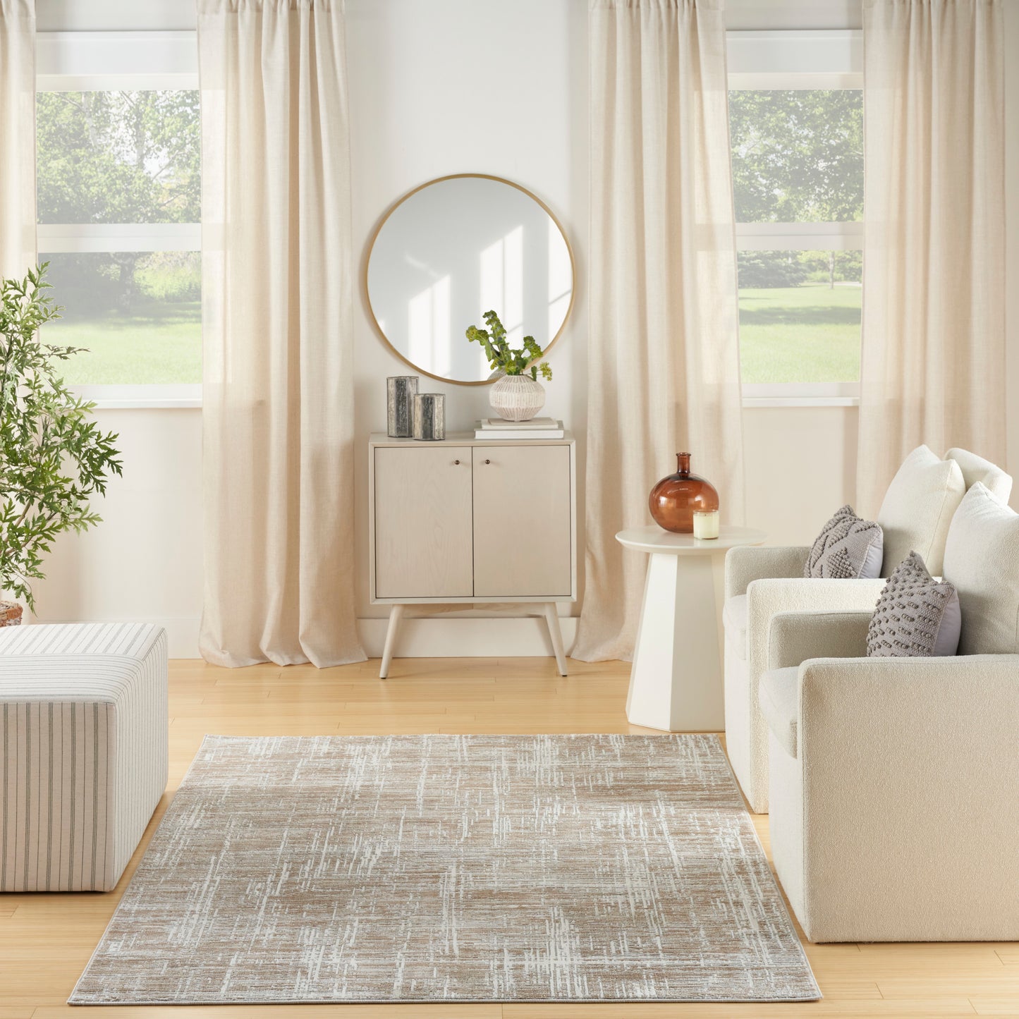 Neutral living room with cream sofa, beige rug, round wall mirror above a white console, light curtains and a plant.