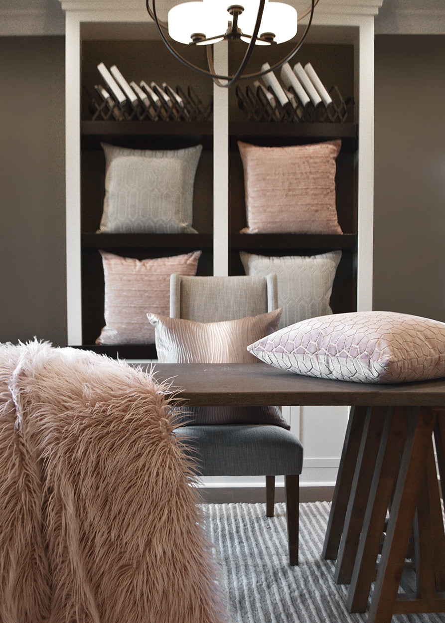 Pink textured Rhythm Pillow in a neutral dining nook with blush and gray cushions, fur throw, wooden table, and chandelier.