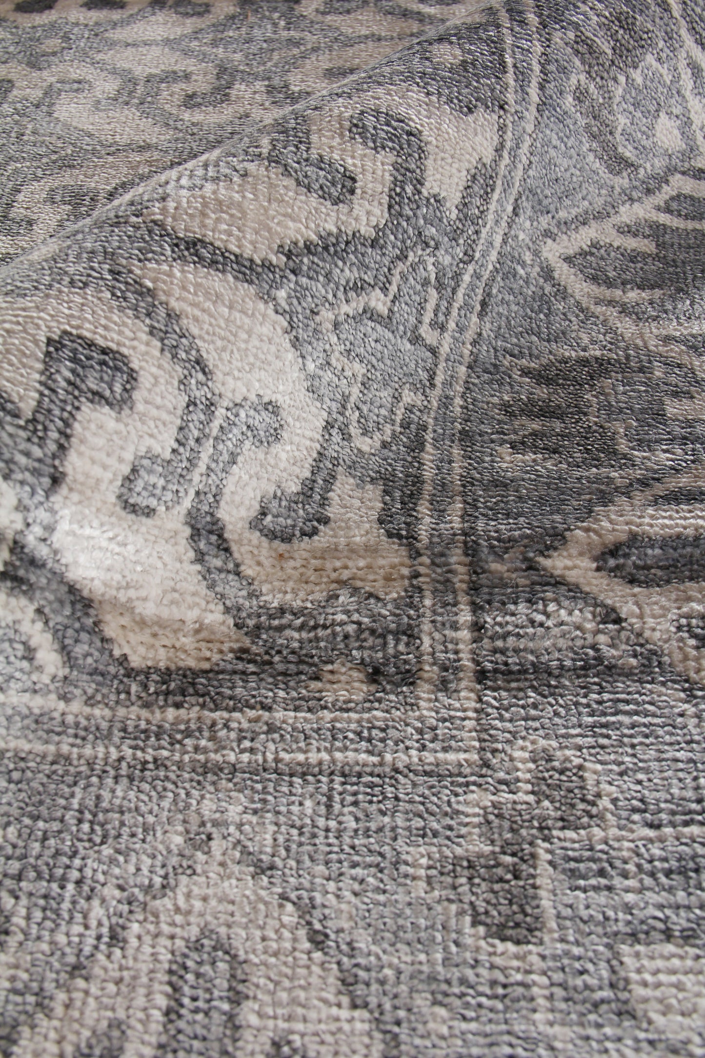 Close-up of gray and beige rug with plush pile and damask-style floral pattern.