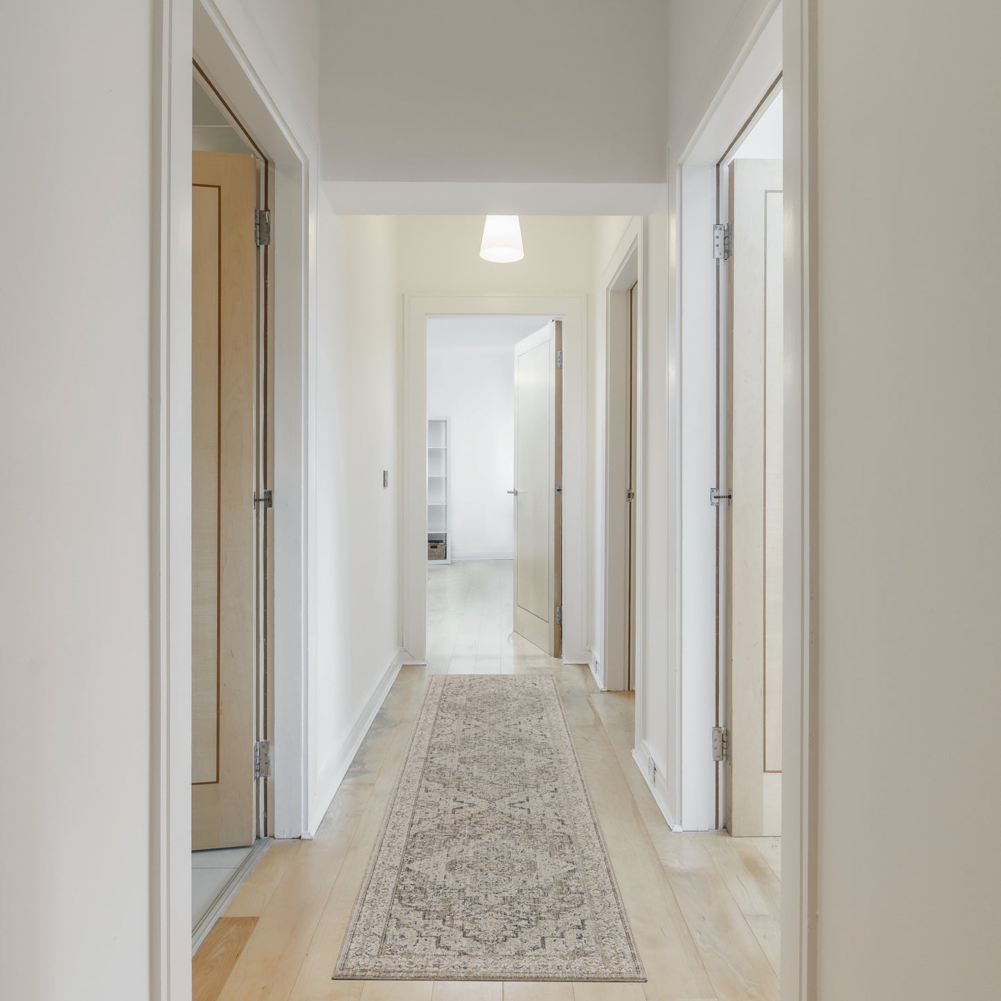 Bright hallway with white walls, light wood doors, a beige patterned runner rug, and a pendant ceiling light.