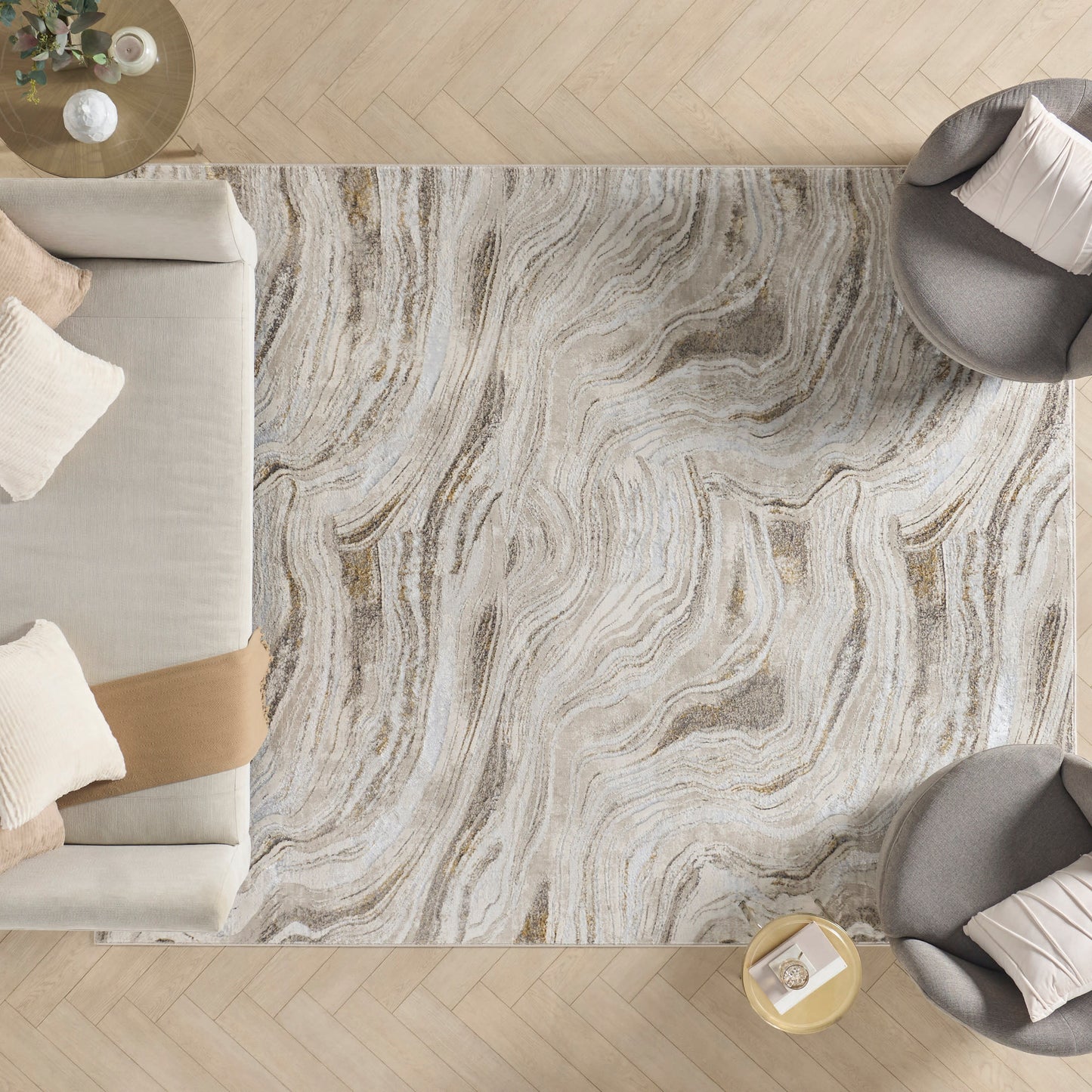 Overhead view of a neutral living room: swirled gray-beige rug, beige sofa, round side table with flowers, and gray chairs.