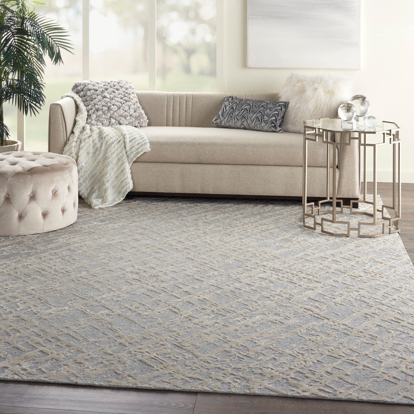 Neutral living room with beige sofa, gray geometric rug, tufted ottoman, plush throws and textured pillows, gold side table.