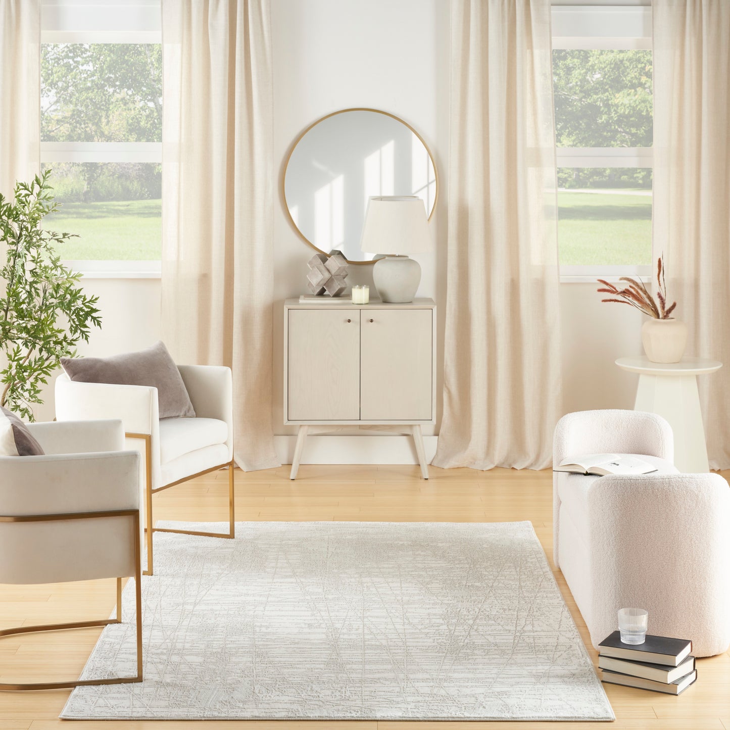 Bright neutral living room with cream seating, light wood cabinet, round mirror, beige curtains, rug, and potted greenery.