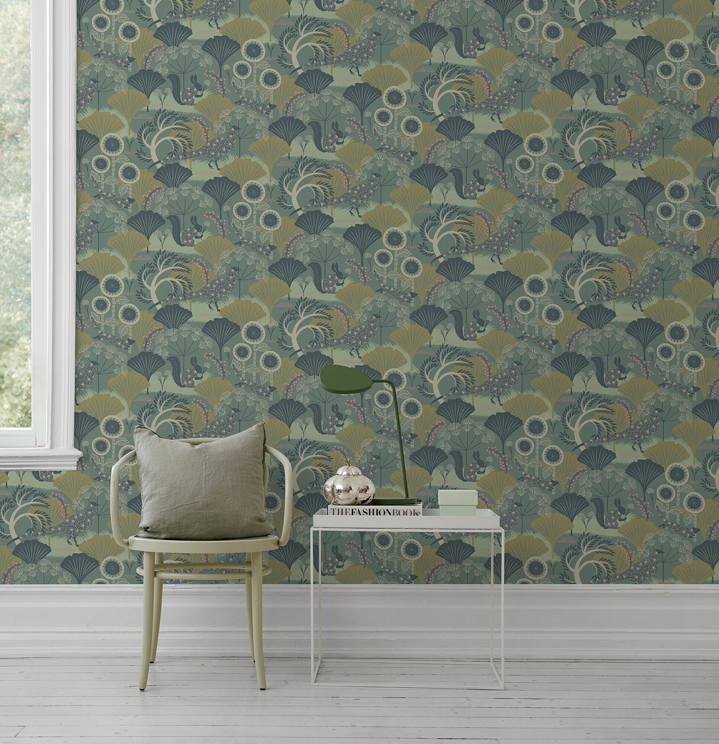 Pale yellow chair with beige cushion beside white metal side table & green desk lamp set against teal botanical wallpaper.