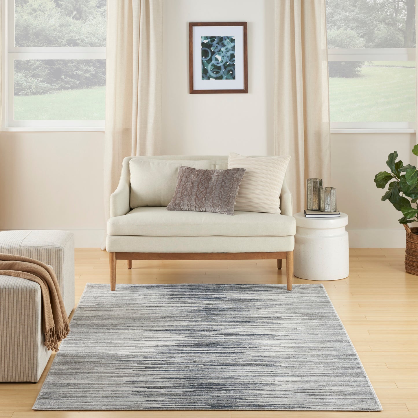 Neutral living room with beige sofa, blue-gray striped rug, cream curtains, framed blue art, and round white side table.