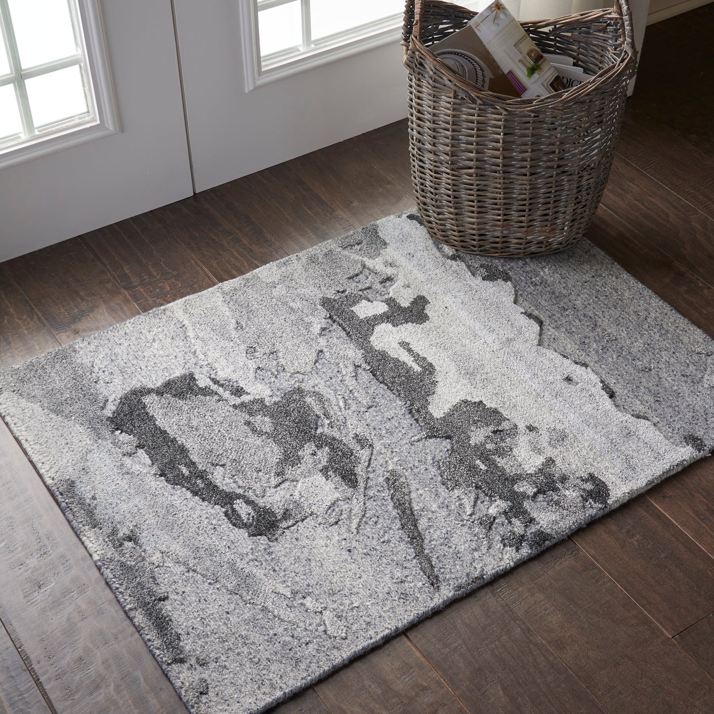 Gray abstract-pattern area rug on dark hardwood floor, near wicker magazine basket.