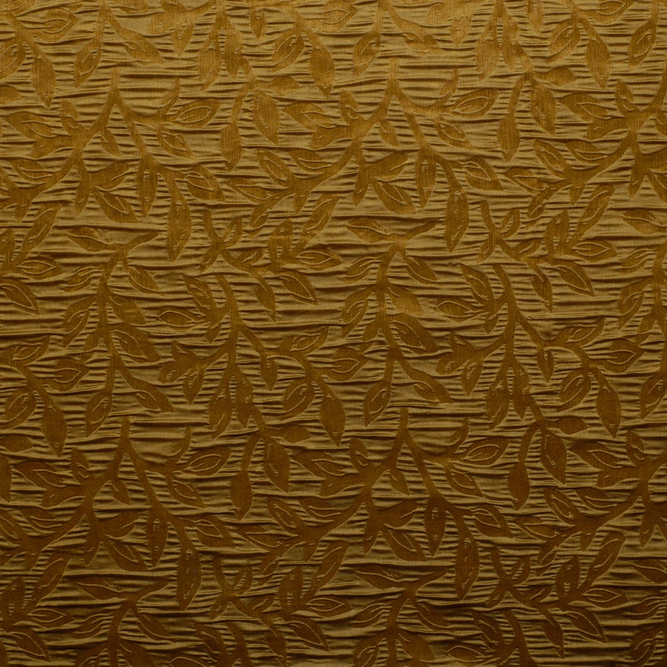 Gold-toned drapery fabric with a subtle bamboo leaf pattern on a textured brown background.