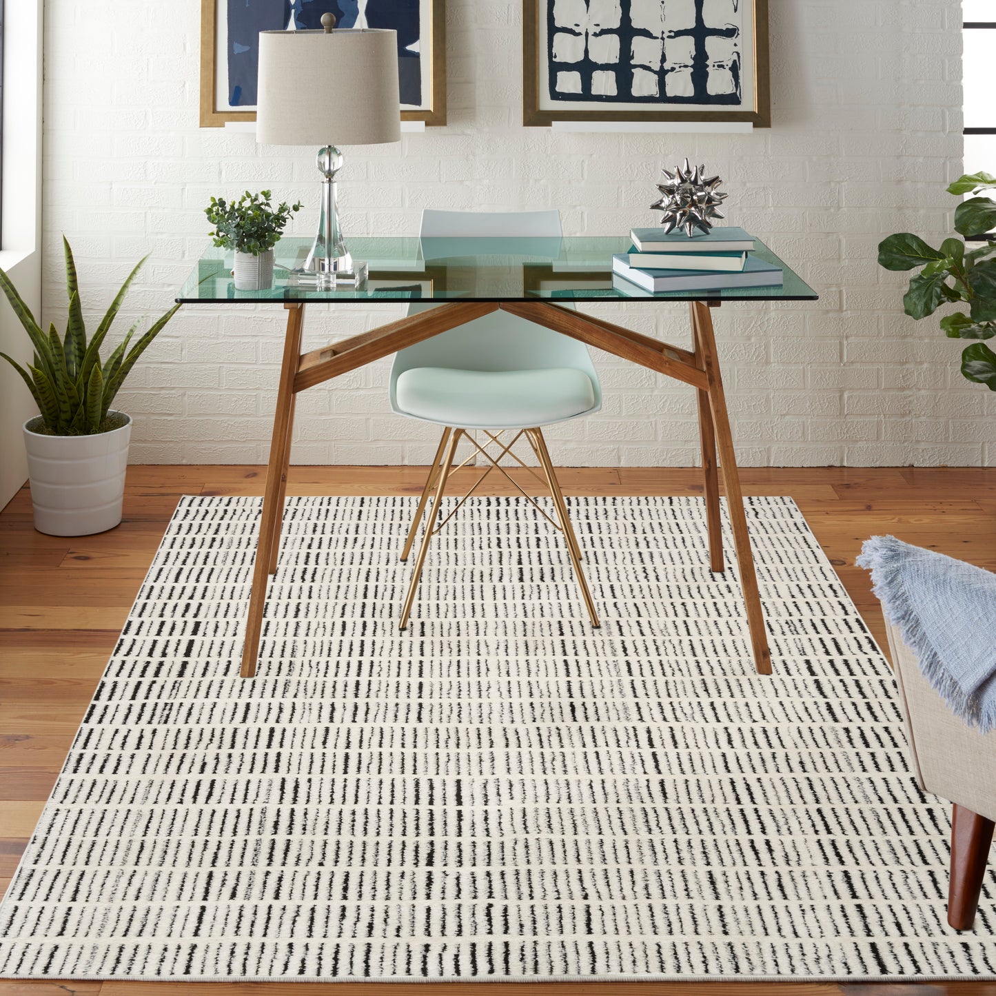 Glass-top desk with wooden legs, mint Eames chair, striped rug, plants, and abstract wall art in a bright home office.