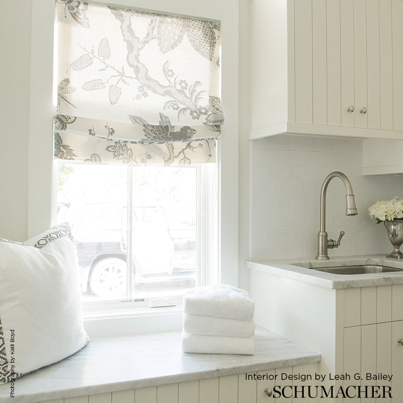 Bright white kitchen with marble countertop window seat, gray botanical roman shade, stacked towels, and stainless sink.