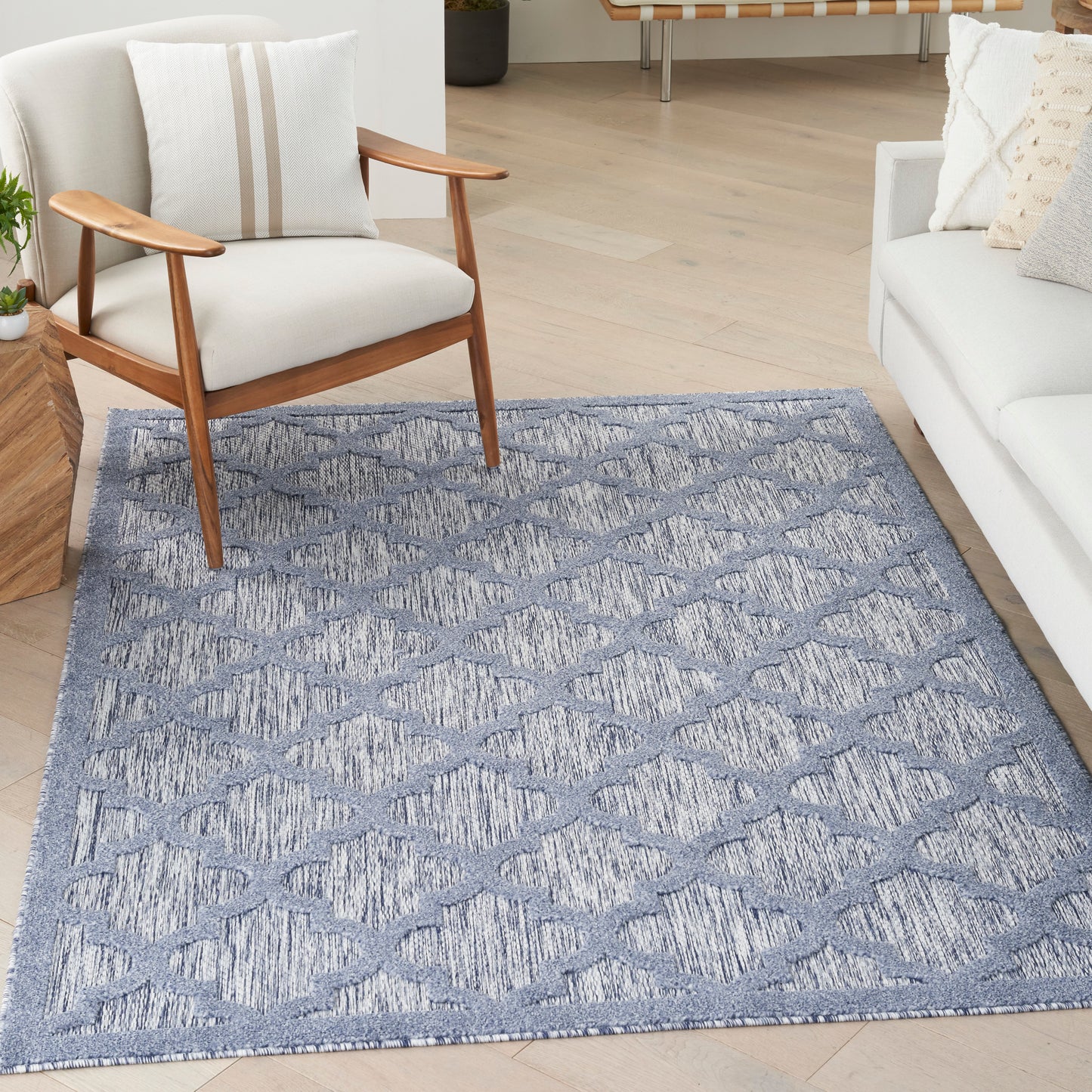 Blue-gray geometric diamond-pattern area rug in a modern living room with a wooden-armchair and white sofa.