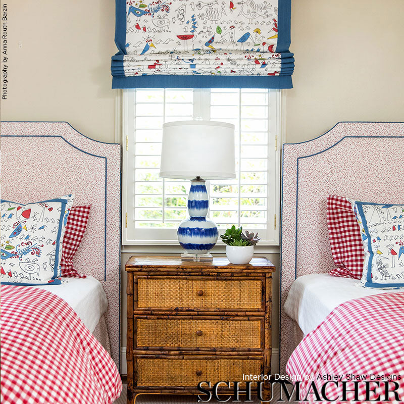 Two twin beds with pink headboards, red gingham quilts, nautical pillows; wood nightstand with blue lamp and plant, blue valance over window.