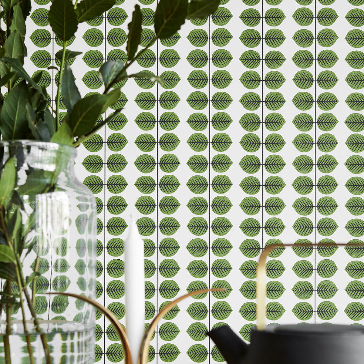 Green leaf-pattern wallpaper with vertical rows; foreground glass vase with stems and a black pot.