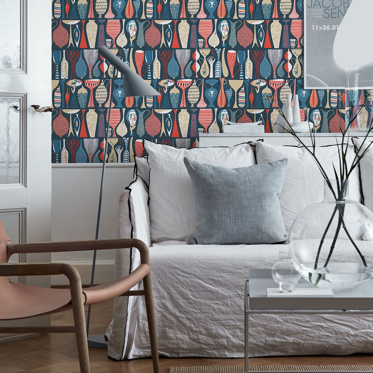Living room with bold blue and red geometric wallpaper, white sofa, gray cushions, arc floor lamp, and glass coffee table.