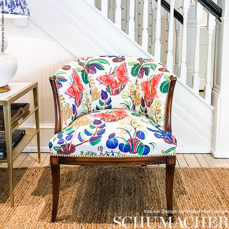 Colorful floral and butterfly upholstered armchair with dark wood legs and brass nailhead trim under a staircase.