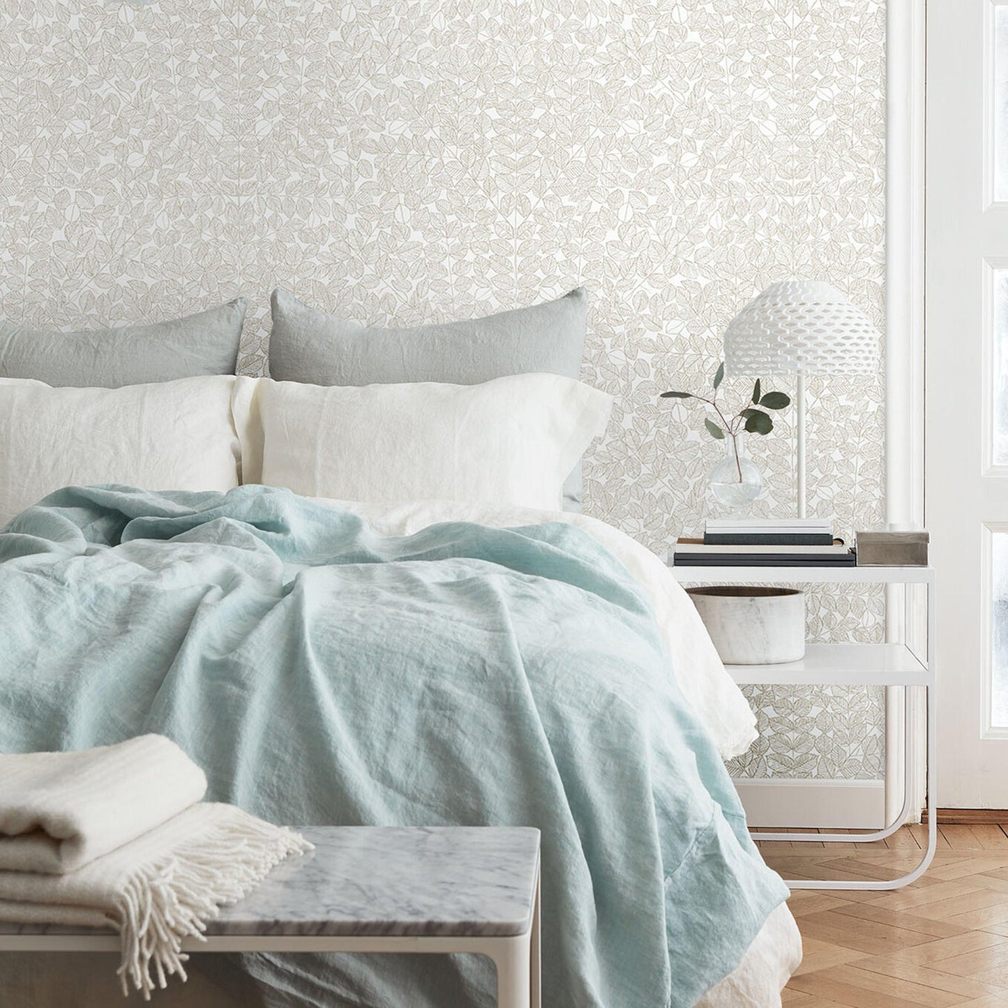 Seafoam duvet with white & gray pillows on a cozy bed, linen texture, pale wallpaper, white side table with lamp.