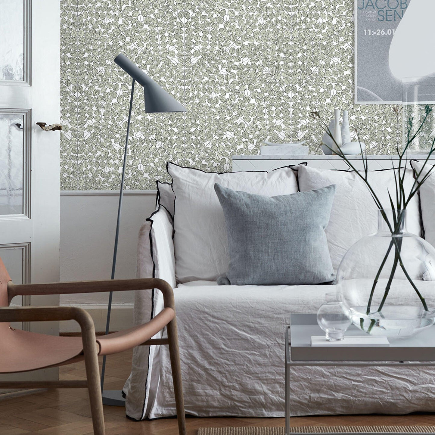 Stylish living room with white slipcovered sofa, pale blue cushions, grey floor lamp, glass coffee table, twig vase.