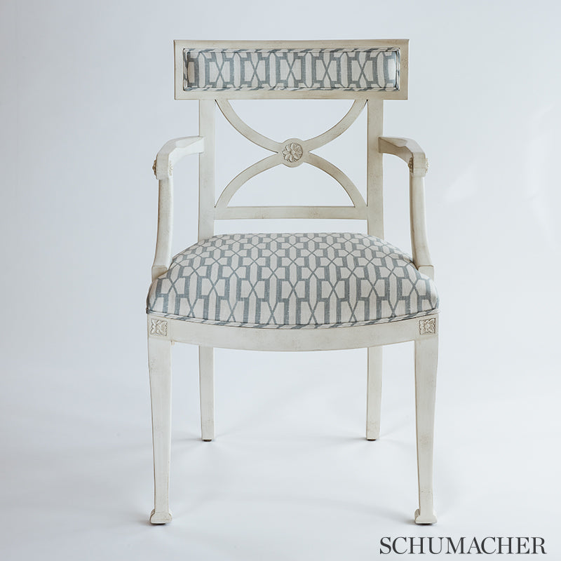 Distressed white wood armchair with blue geometric upholstery on seat and back, carved back panel and tapered legs.