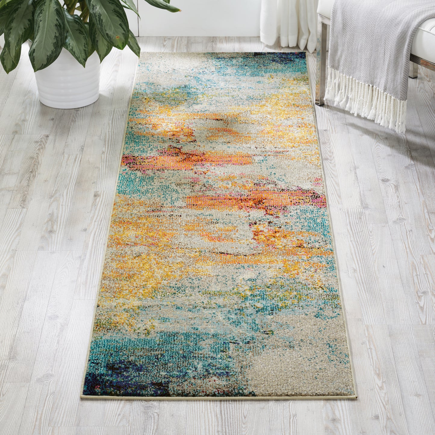 Abstract multicolor area rug with warm and cool tones on light wood floor, in bright room with plant.