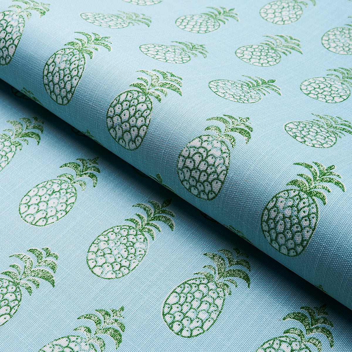 Light blue fabric with a repeating green pineapple print, folded on a roll.