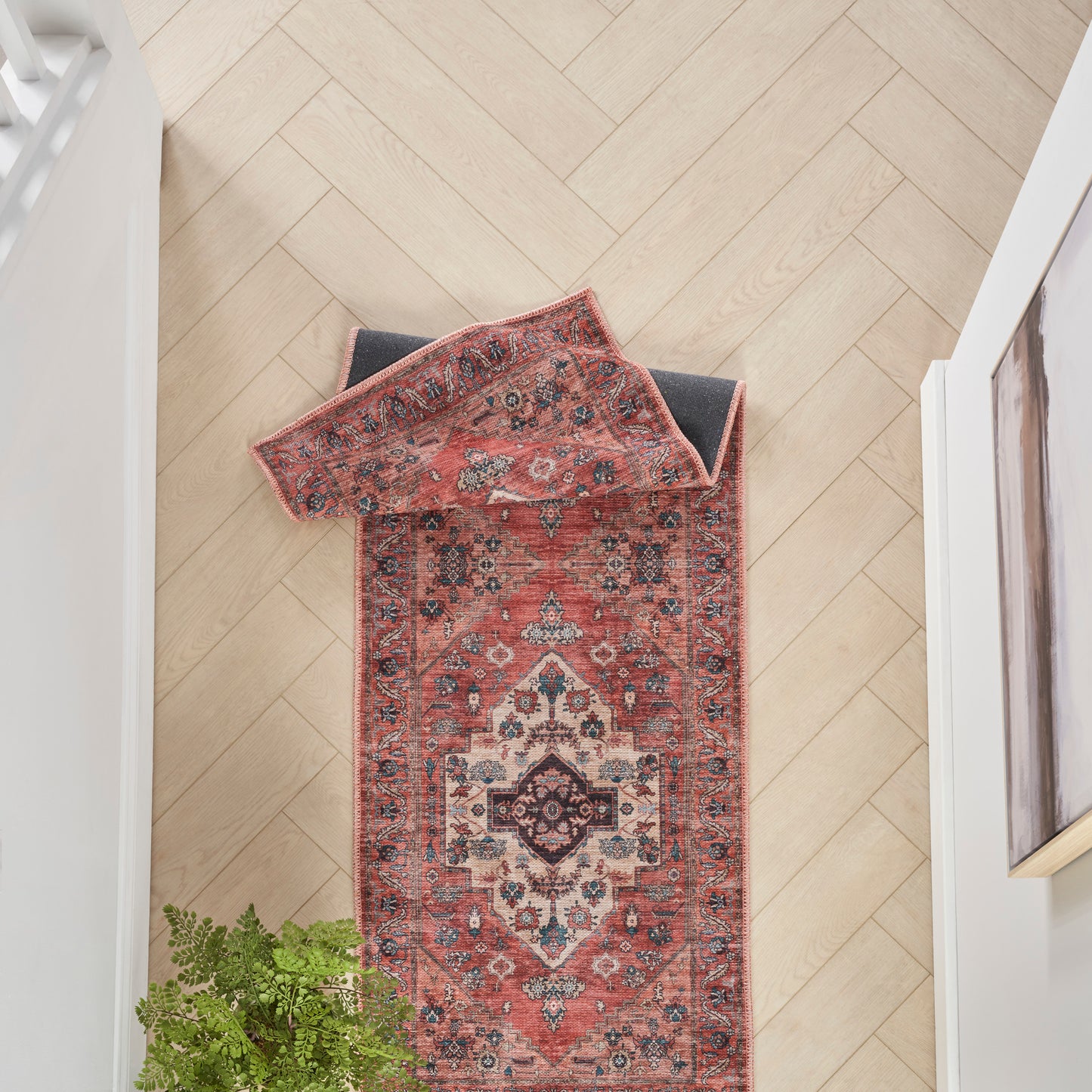 Persian-style red runner rug with central medallion and intricate borders on a light wood herringbone hallway floor.