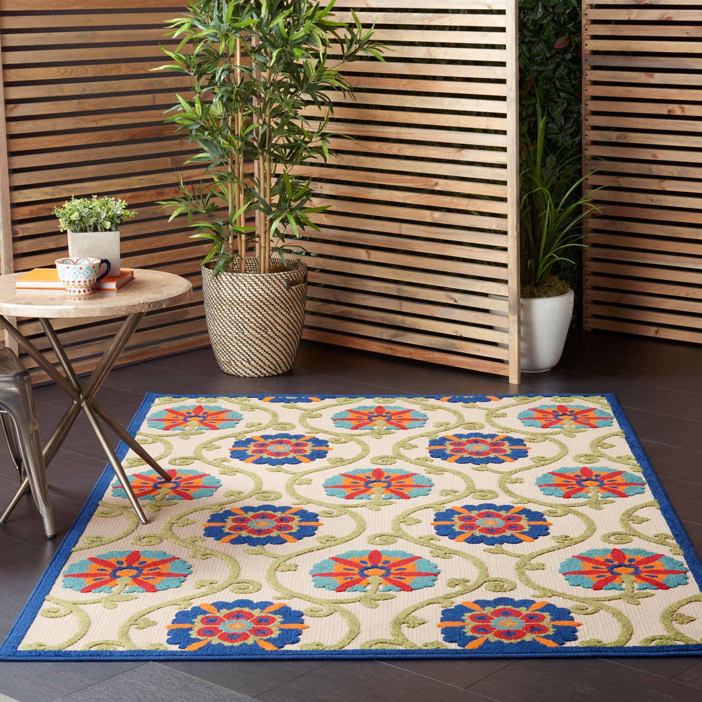 Rectangular 5' x 8' outdoor woven rug with beige field, blue border and red-blue floral medallions; patio decor.