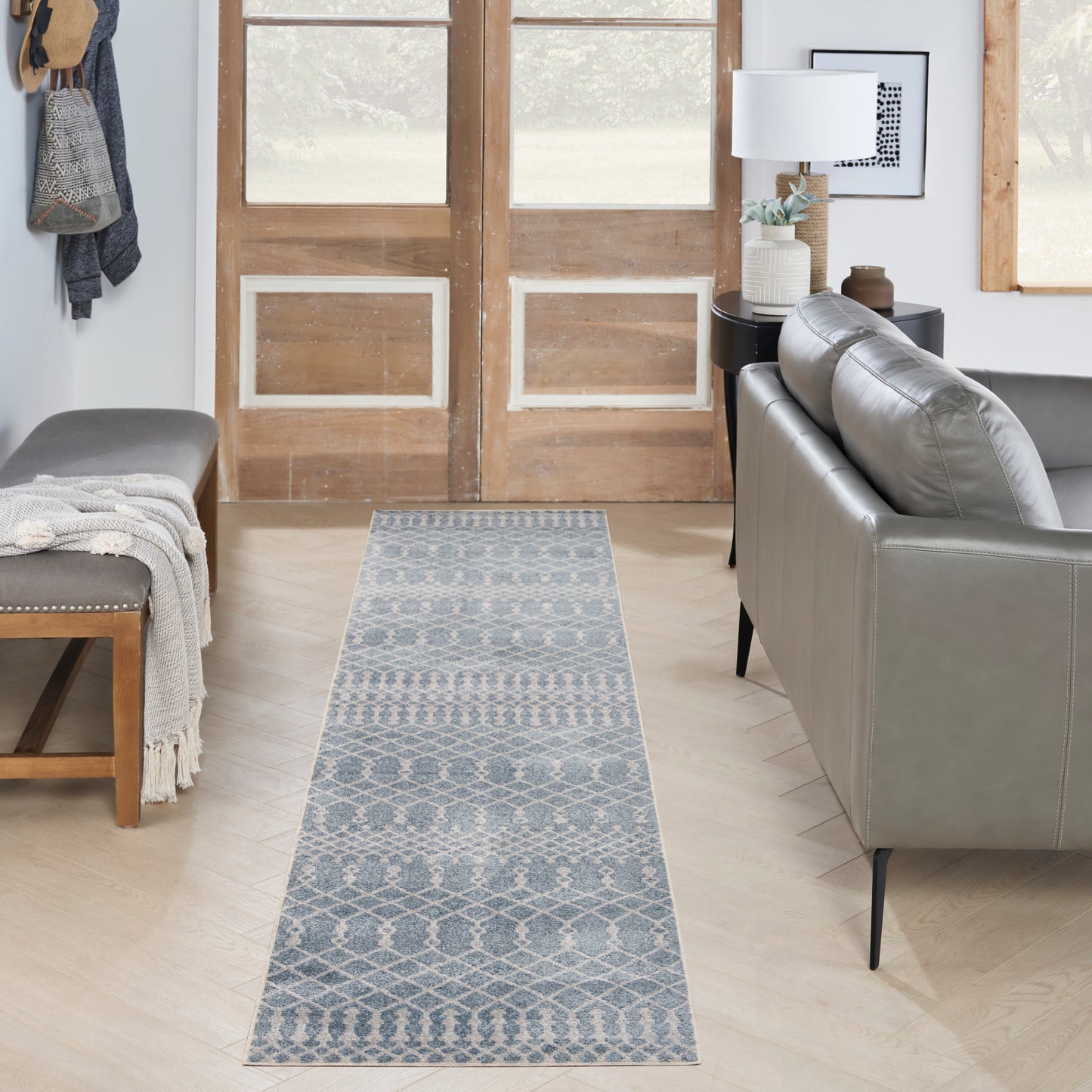 Blue-gray geometric runner rug on light wood floor in a cozy living room with a gray sofa and wooden double doors.