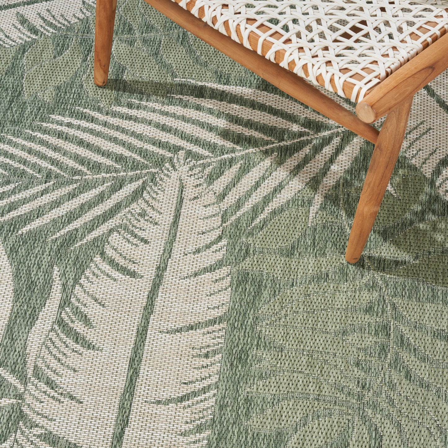 Green palm-leaf patterned woven rug on beige base with a wooden chair and white woven seat.