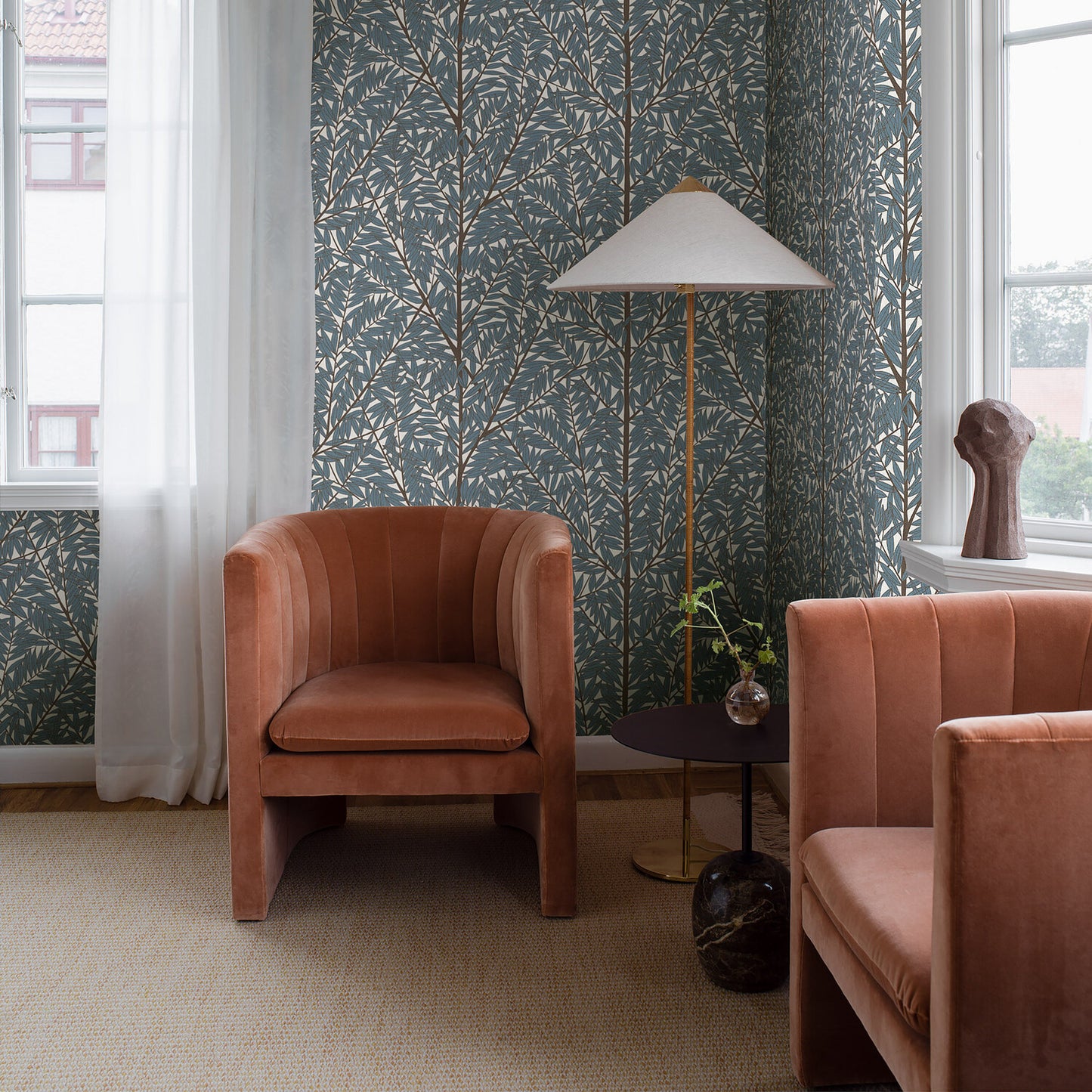 Dusty rose velvet lounge chairs with curved arms, brass floor lamp, round table, teal botanical wallpaper, natural light.