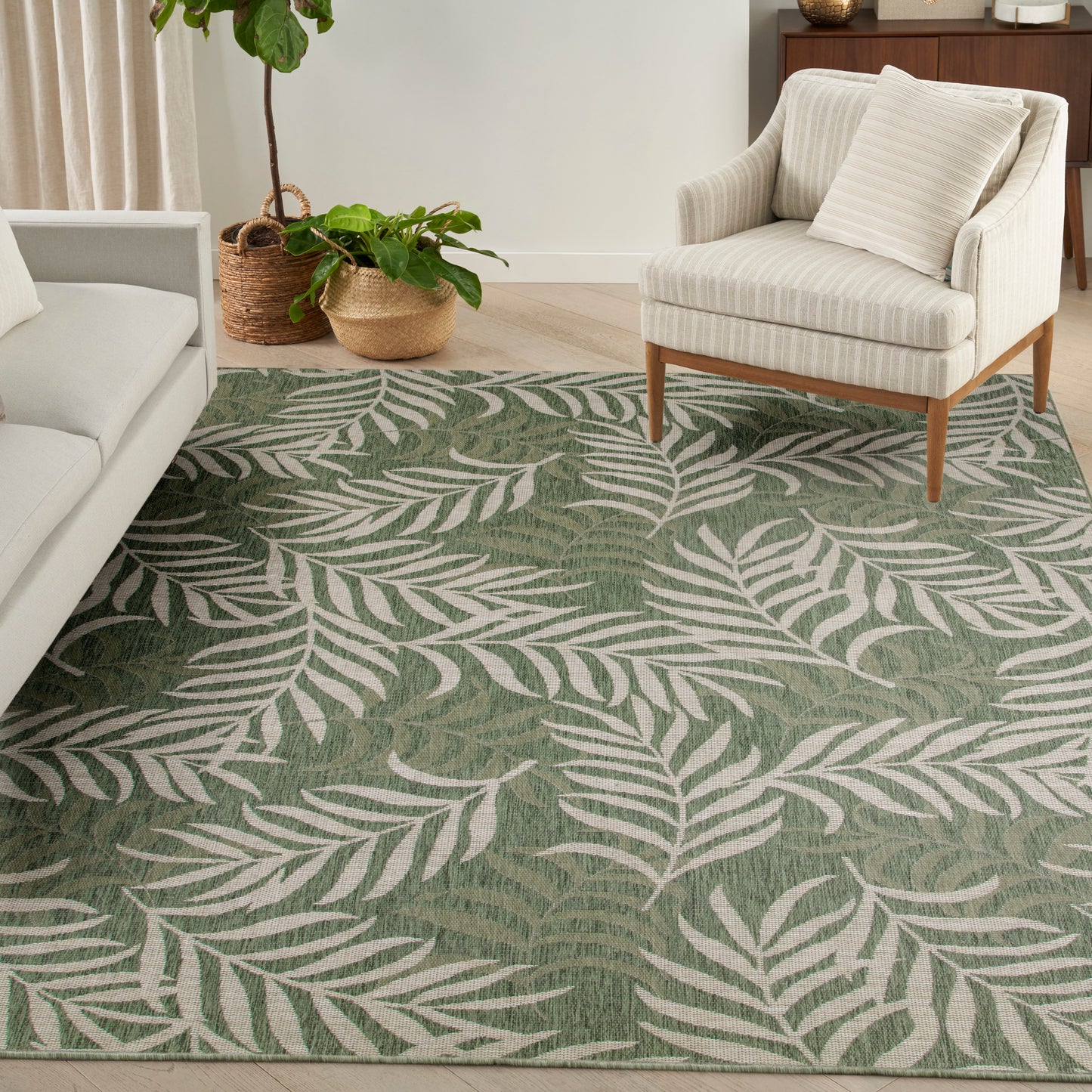 Green area rug with white fern leaves; cozy living room with beige sofa, cream armchair and potted plants.