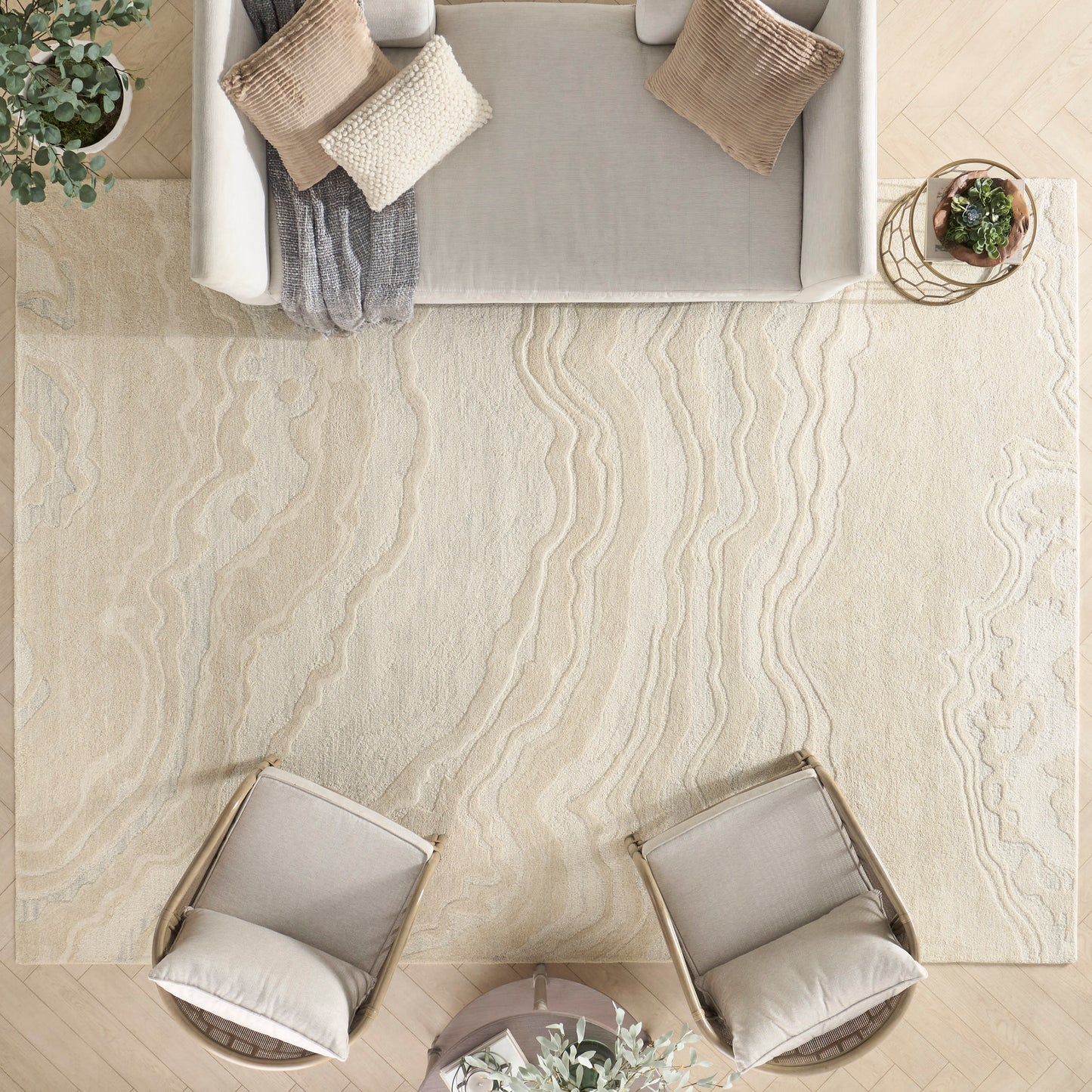 Beige textured rug with wavy cream pattern; gray sofa, two armchairs, round glass coffee table, plants.