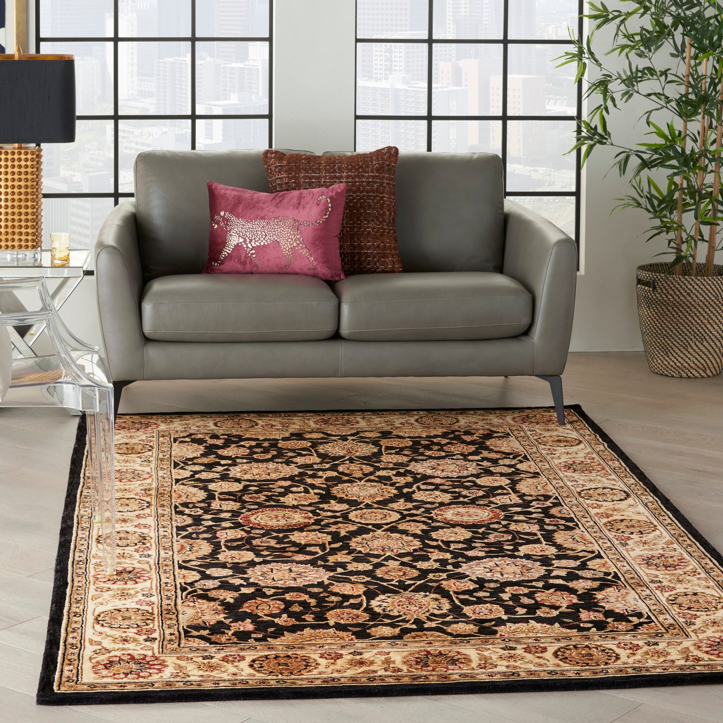 Grey leather loveseat with pink and brown cushions; black-and-cream oriental rug in a bright city living room.