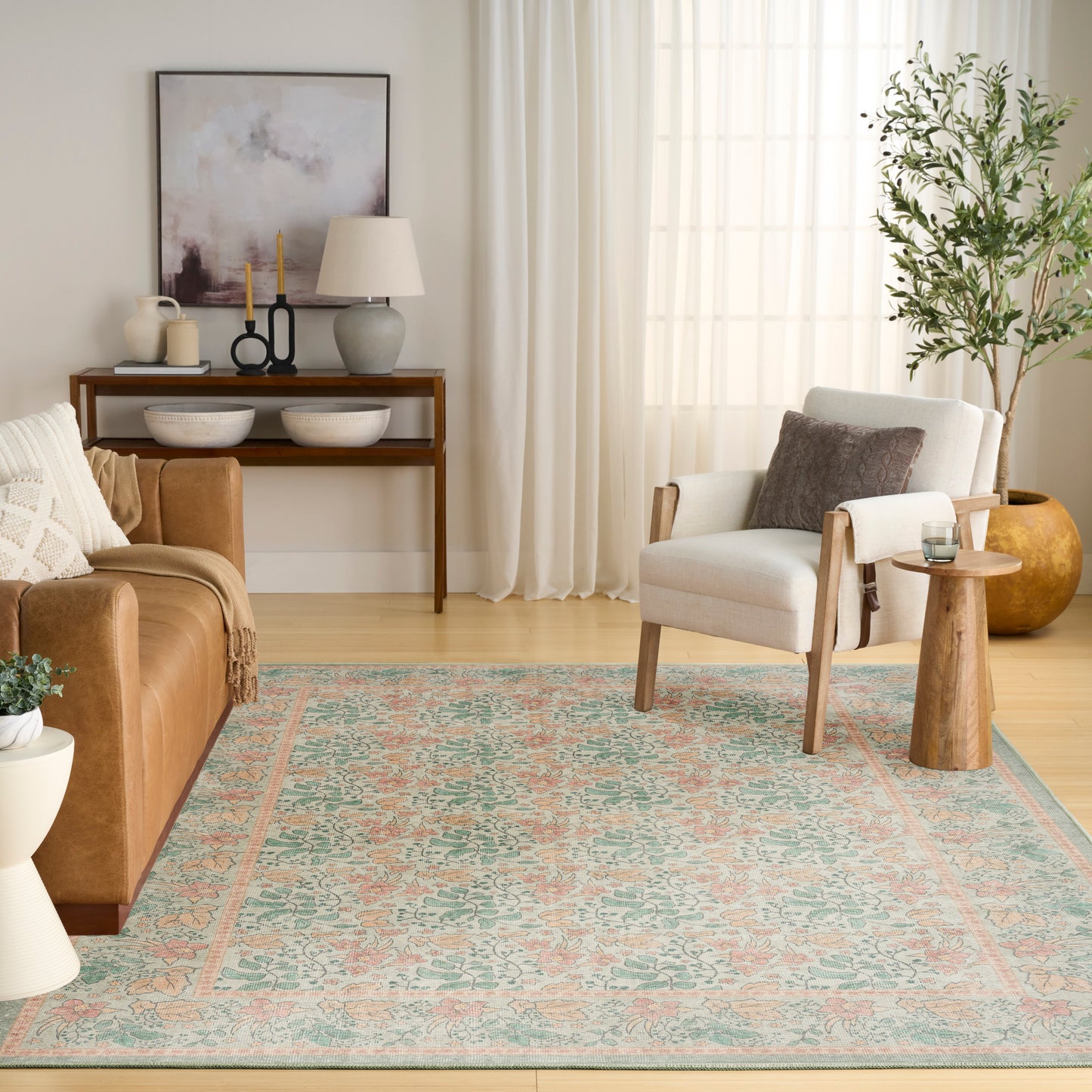 Living room with teal and peach patterned rug, tan leather sofa, light gray armchair, wooden console, framed art, and plant.