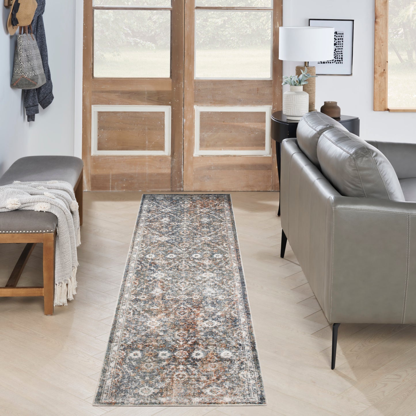 Long woven runner rug with vintage floral medallion in blue, ivory, gray and rust; sets the entryway beside a gray sofa.
