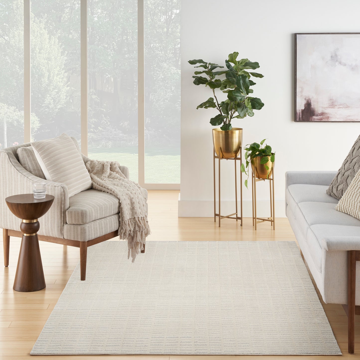 Neutral living room with beige rug, light gray sofa, cream armchair, brass plant stands and lush green plants