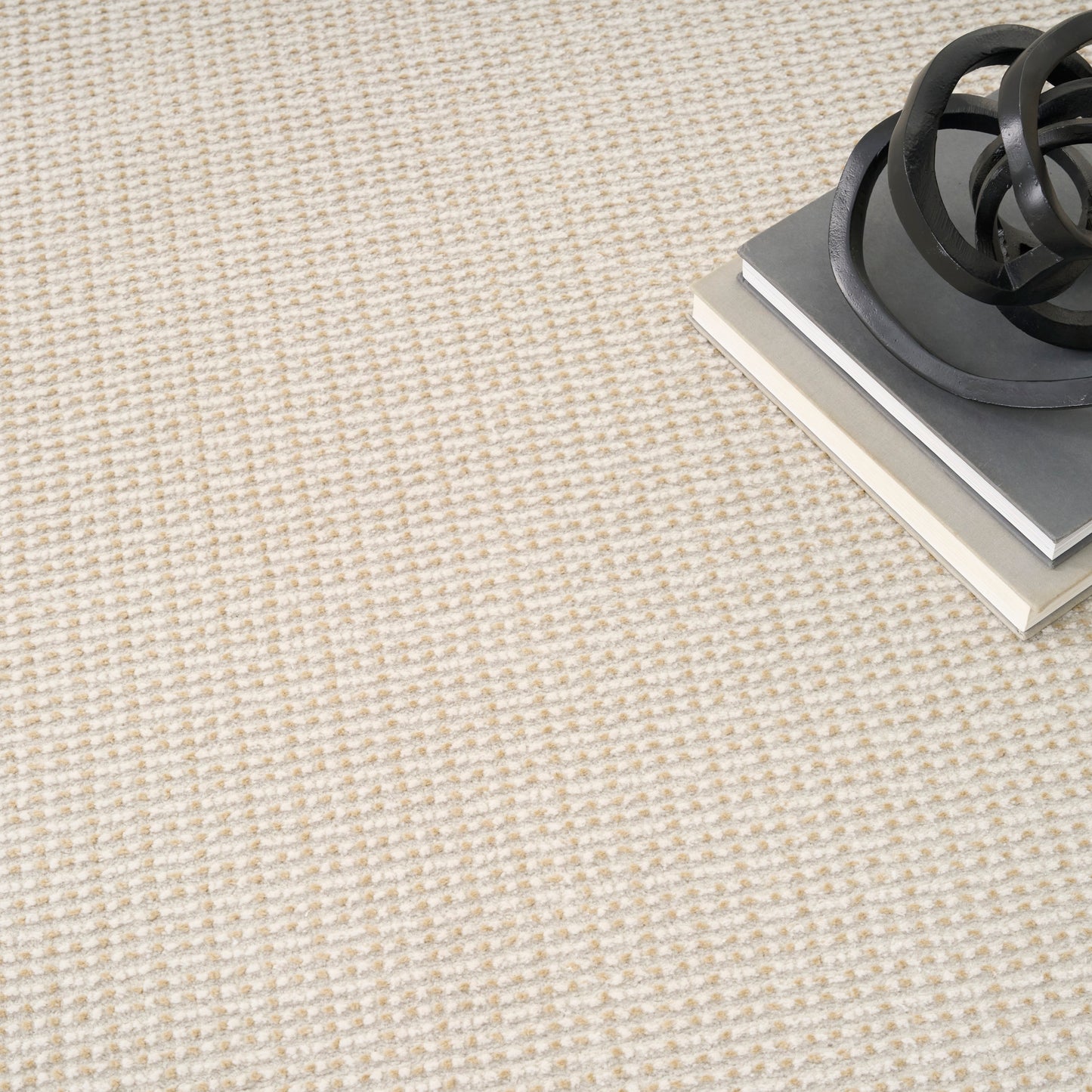 Beige textured carpet with a stack of gray books topped by a black metal spiral sculpture.