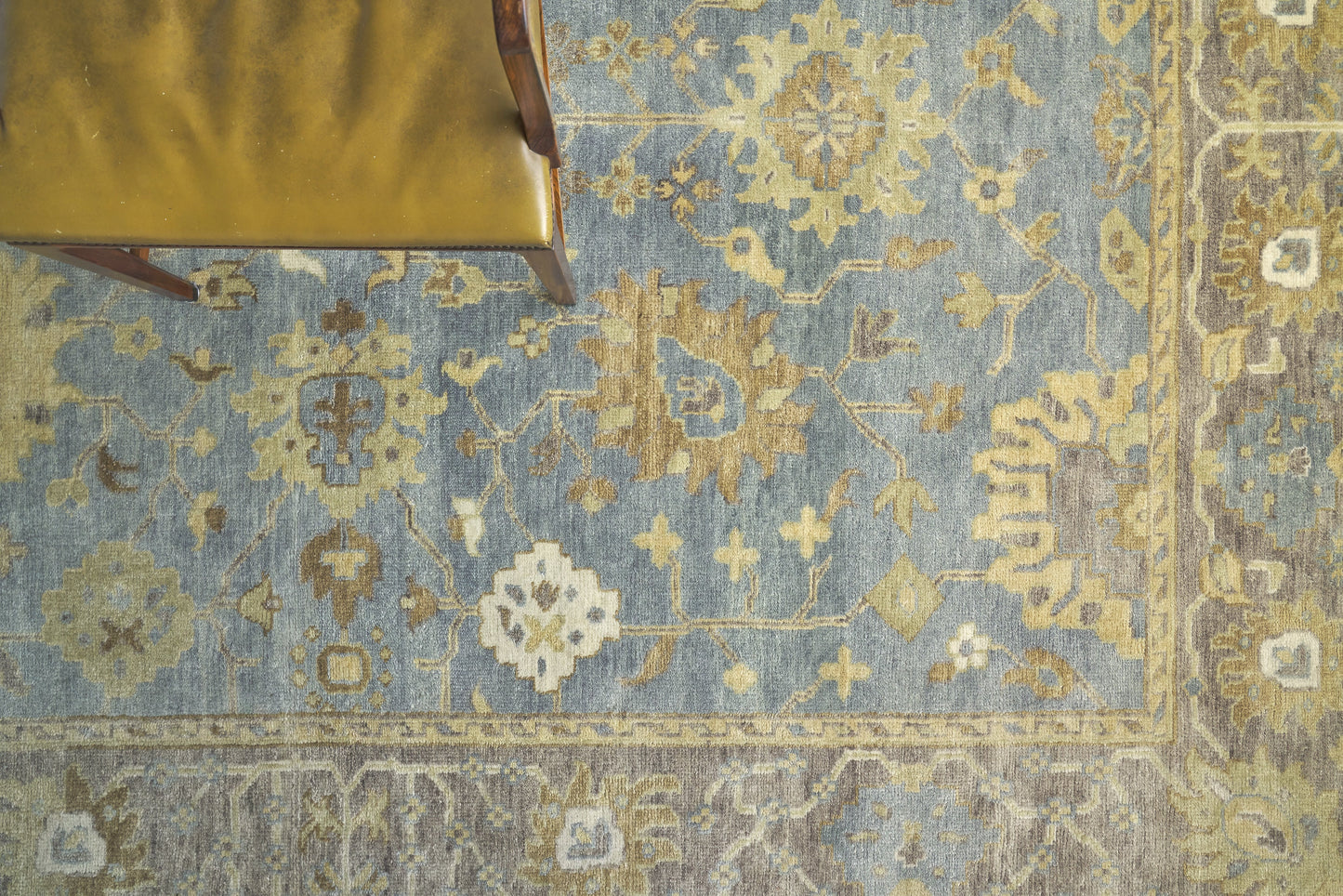 Blue oriental rug with gold-beige floral pattern and border; mustard-yellow chair leg visible in top-left.