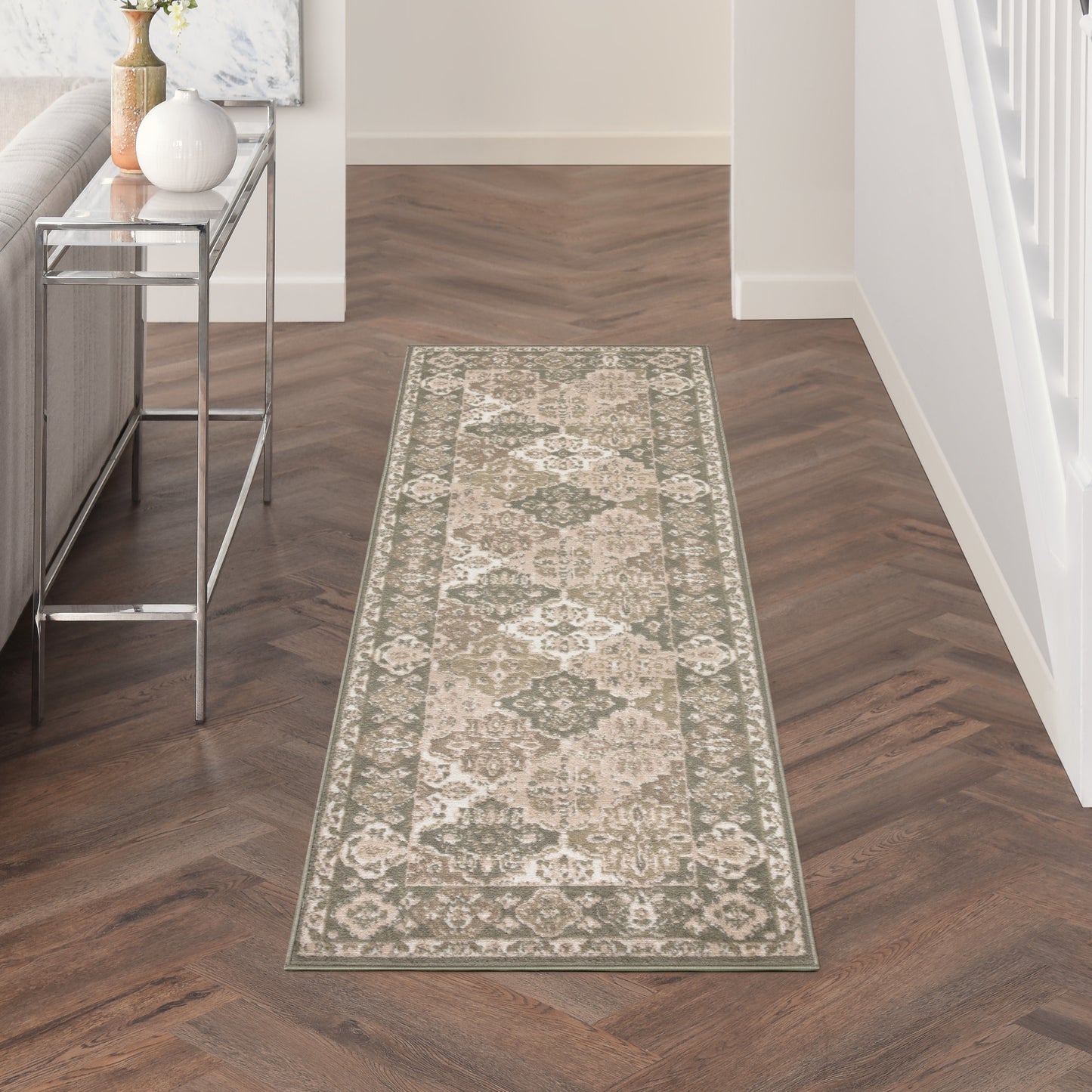 Beige-and-gray oriental rug runner on a dark herringbone hallway floor beside a metal console table with a vase.